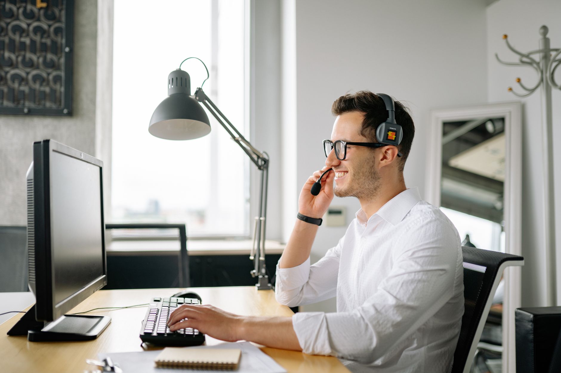 Smiling man wearing headset working at computer in bright office — illustrating: VoIP vs Traditional Phone Systems in Central Florida: Which Saves Your SMB More Money in 2025?
